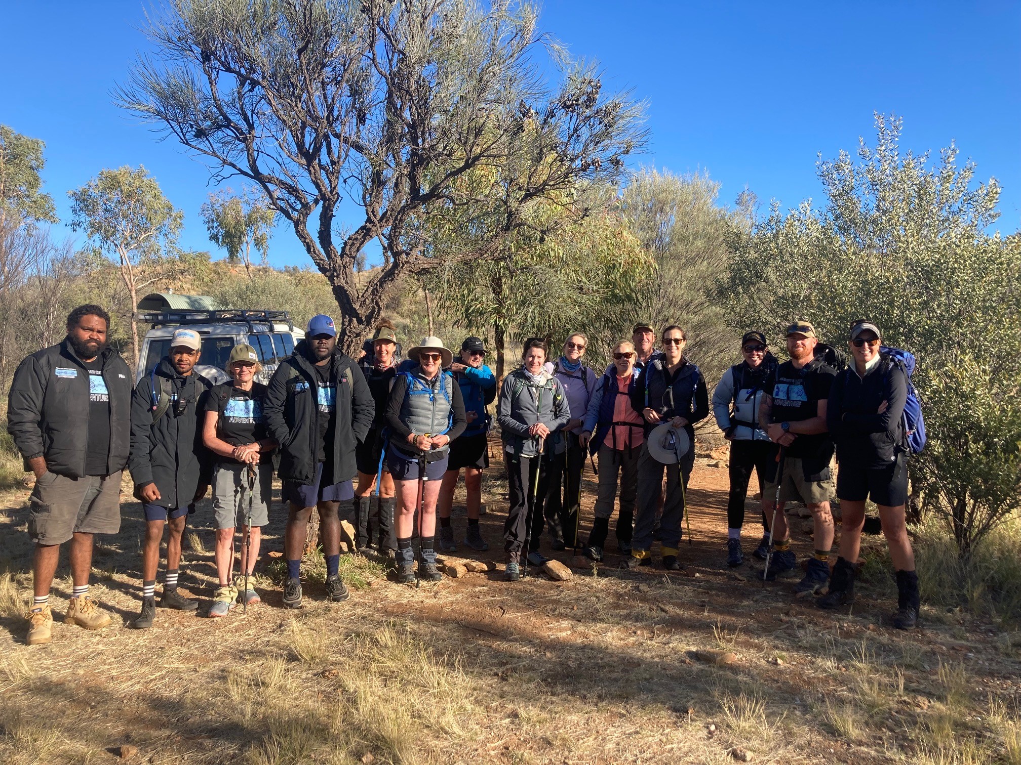 A group of travellers and First Nations guides from 100% Finke River Culture & Adventure stand together at the start of a day’s hike on the Larapinta Trail. An immersive walking experience through Tjoritja (West MacDonnell Ranges) with Inspiration Outdoors.