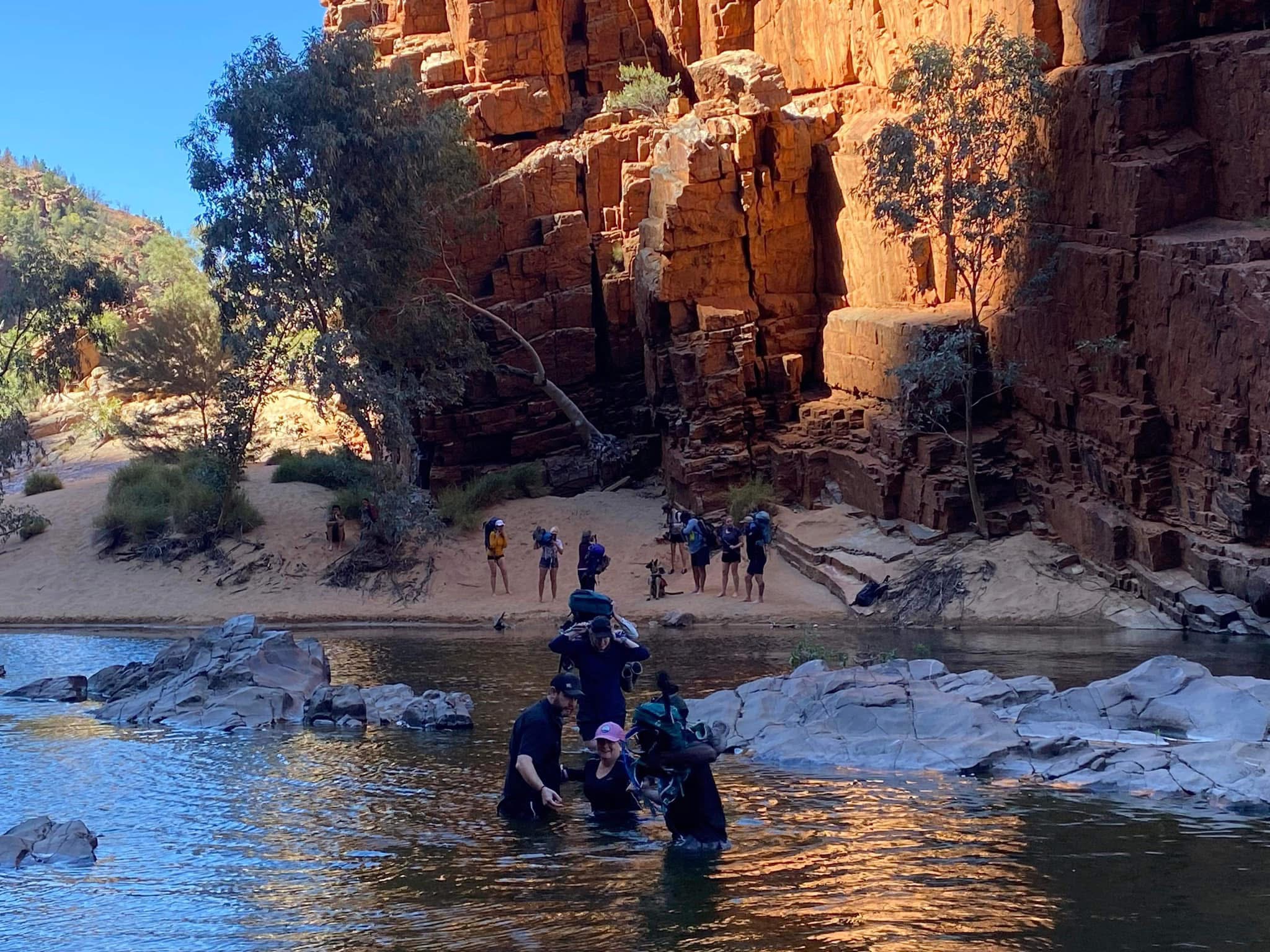 Travellers cool off in a tranquil waterhole along the Larapinta Trail, surrounded by towering red cliffs and ancient rock formations. Guided by First Nations leaders from 100% Finke River Culture & Adventure, this moment captures the spirit of connection to Country with Inspiration Outdoors.