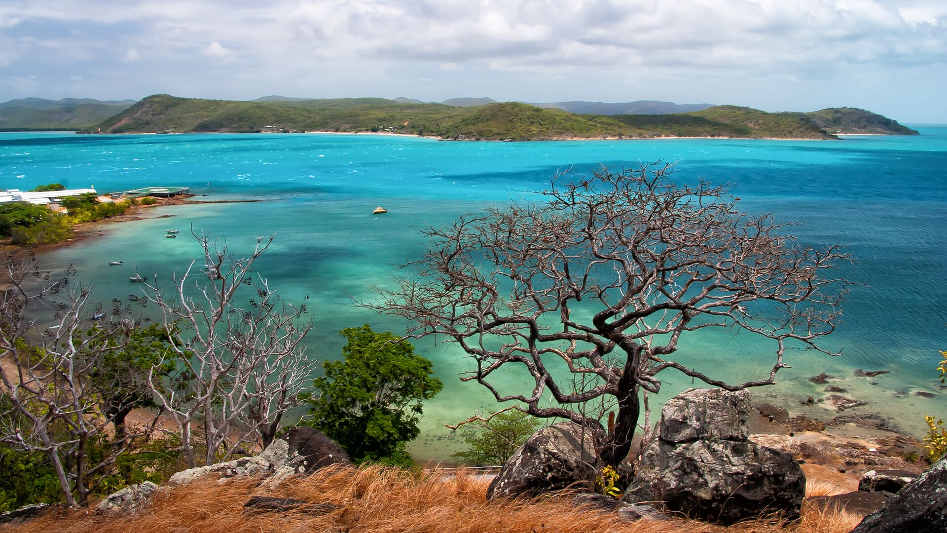 A stunning view of the vibrant turquoise waters surrounding Thursday Island in the Torres Strait, Queensland, with rocky cliffs, windswept trees, and distant islands under a partly cloudy sky with inspiration outdoors